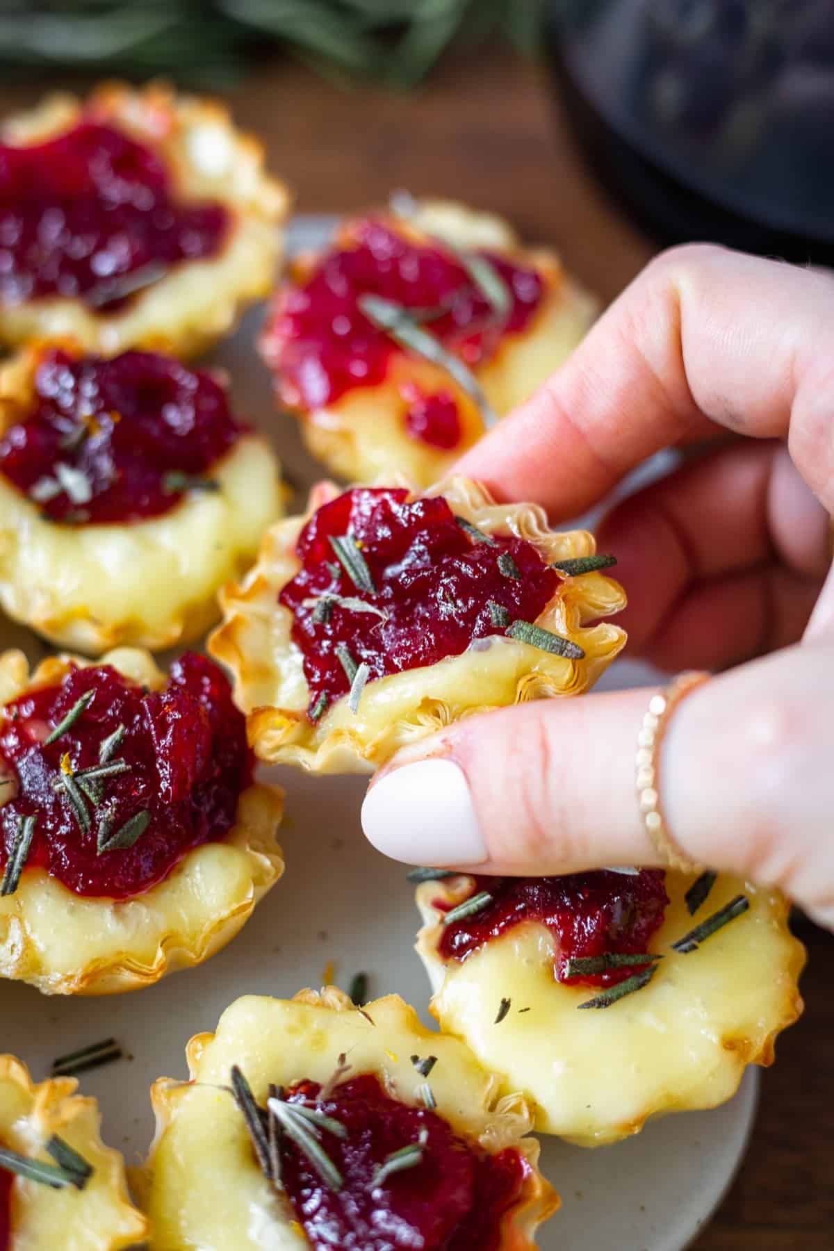 Flaky phyllo cups stuffed with melty brie and gooey cranberry being grabbed by a hand
