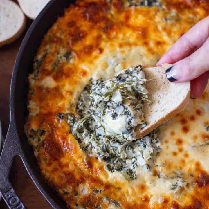 Dipping a piece of bread in cheesy spinach artichoke dip