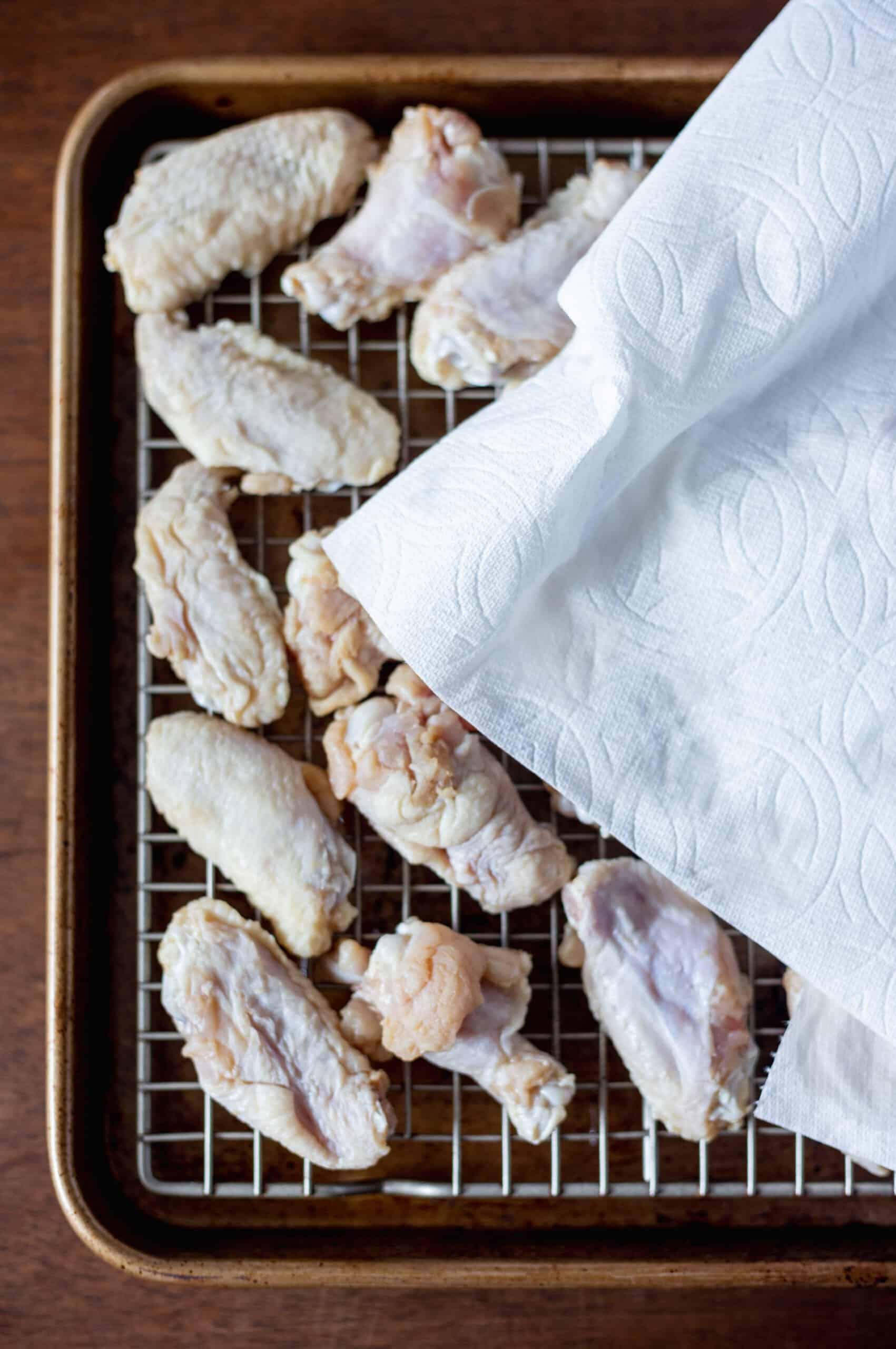 Chicken wings being dried with paper towel on a sheet pan