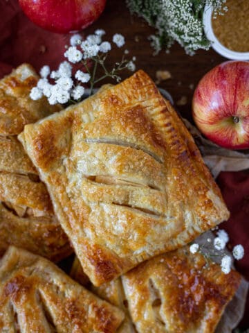 An apple hand pie with puff pastry surrounded by apples and floral