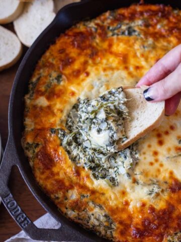 Dipping a piece of bread in cheesy spinach artichoke dip
