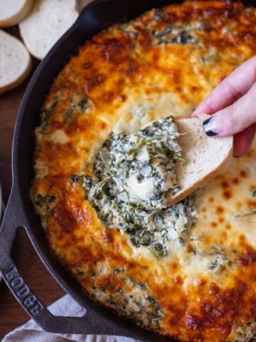 Dipping a piece of bread in cheesy spinach artichoke dip