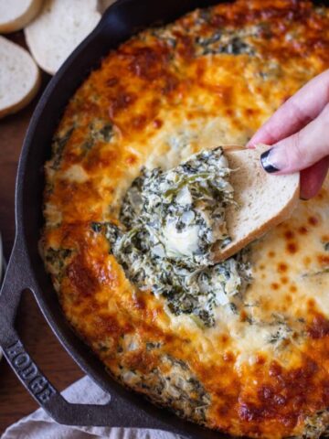Dipping a piece of bread in cheesy spinach artichoke dip