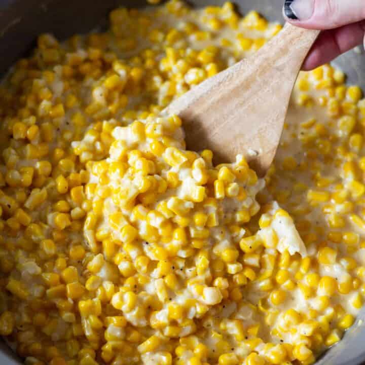 Large saucepan filled with creamed corn and a spoon