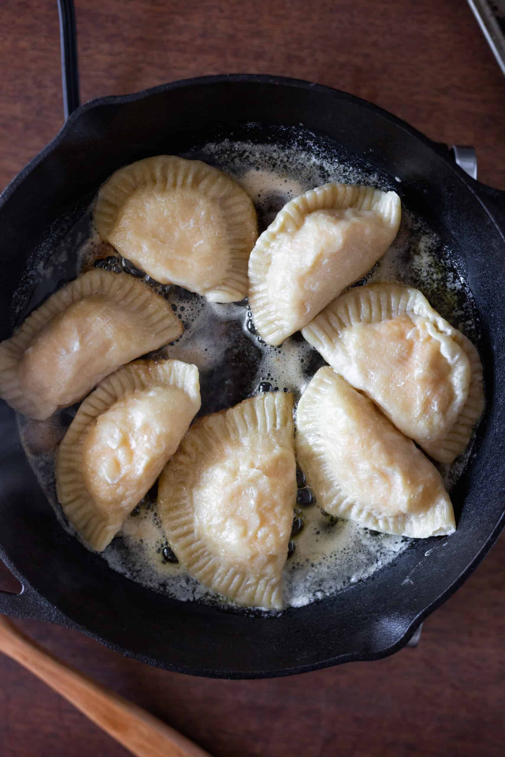 Pierogi being sauteed in a large skillet with butter