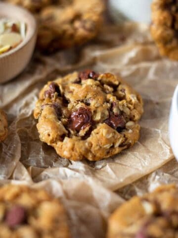A oatmeal chocolate chip cookie surrounded by other cookies and milk