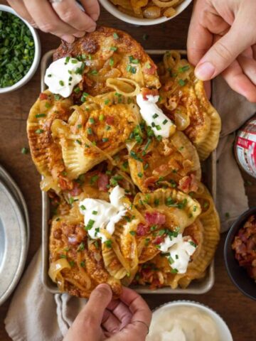 Large platter of pierogi with lots of toppings and hands in the picture