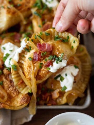 A single pierogi being held with all the toppings