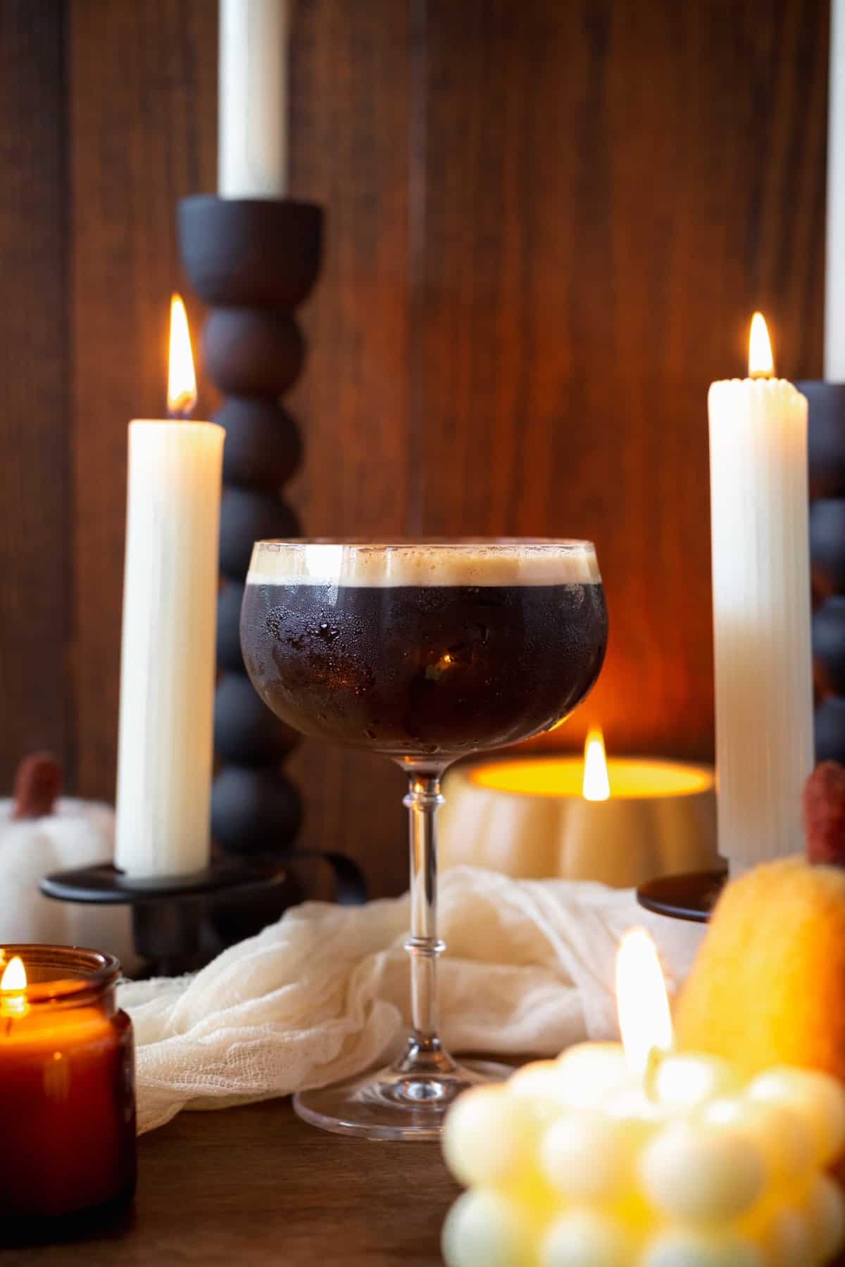 a martini glass filled with pumpkin espresso martini cocktail surrounded by candles and pumpkins