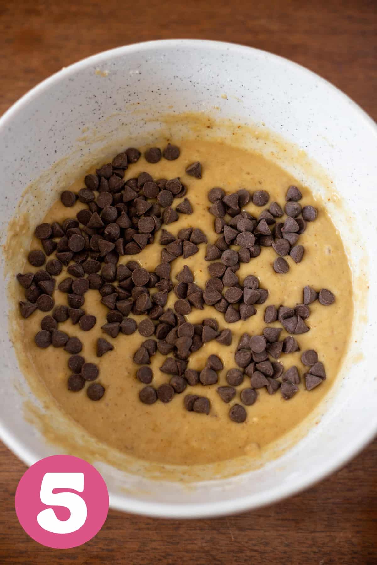 A large bowl of combine banana bread batter with chocolate chips sprinkled in