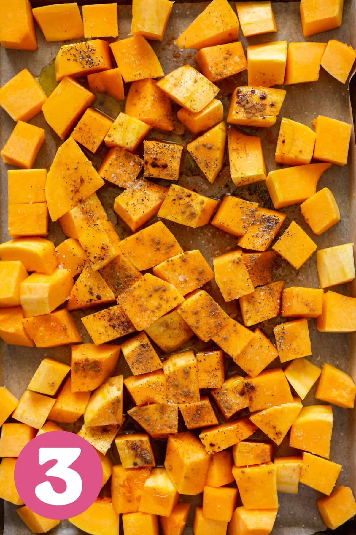 cubed butternut squash tossed in oils and seasonings on a tray