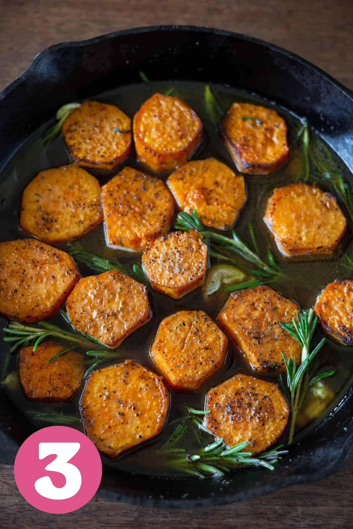 A cast iron pan of fondant sweet potatoes with chicken broth and rosemary