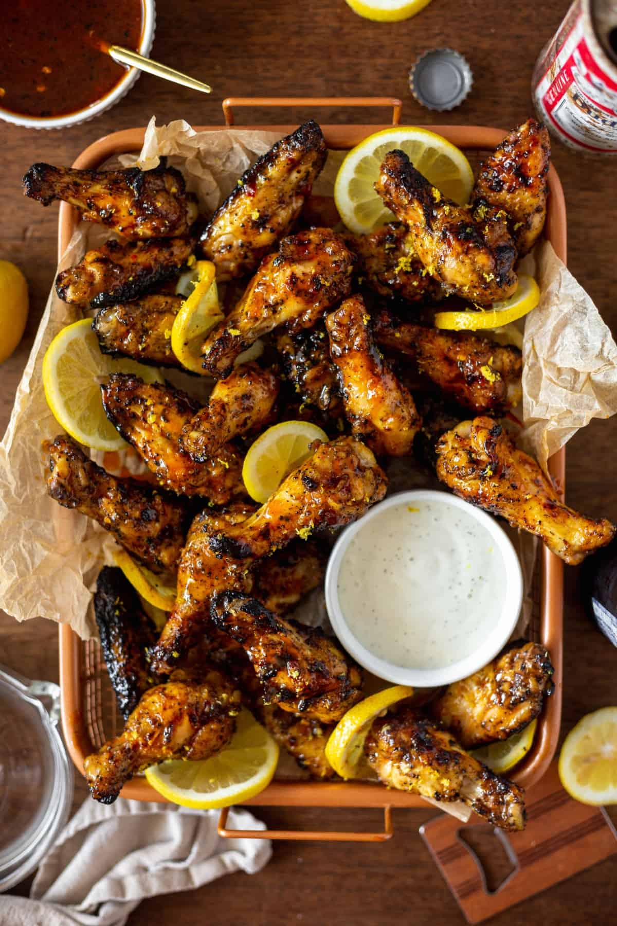 large orange platter of hot honey lemon pepper chicken wings with lemons spread all over and a side of ranch