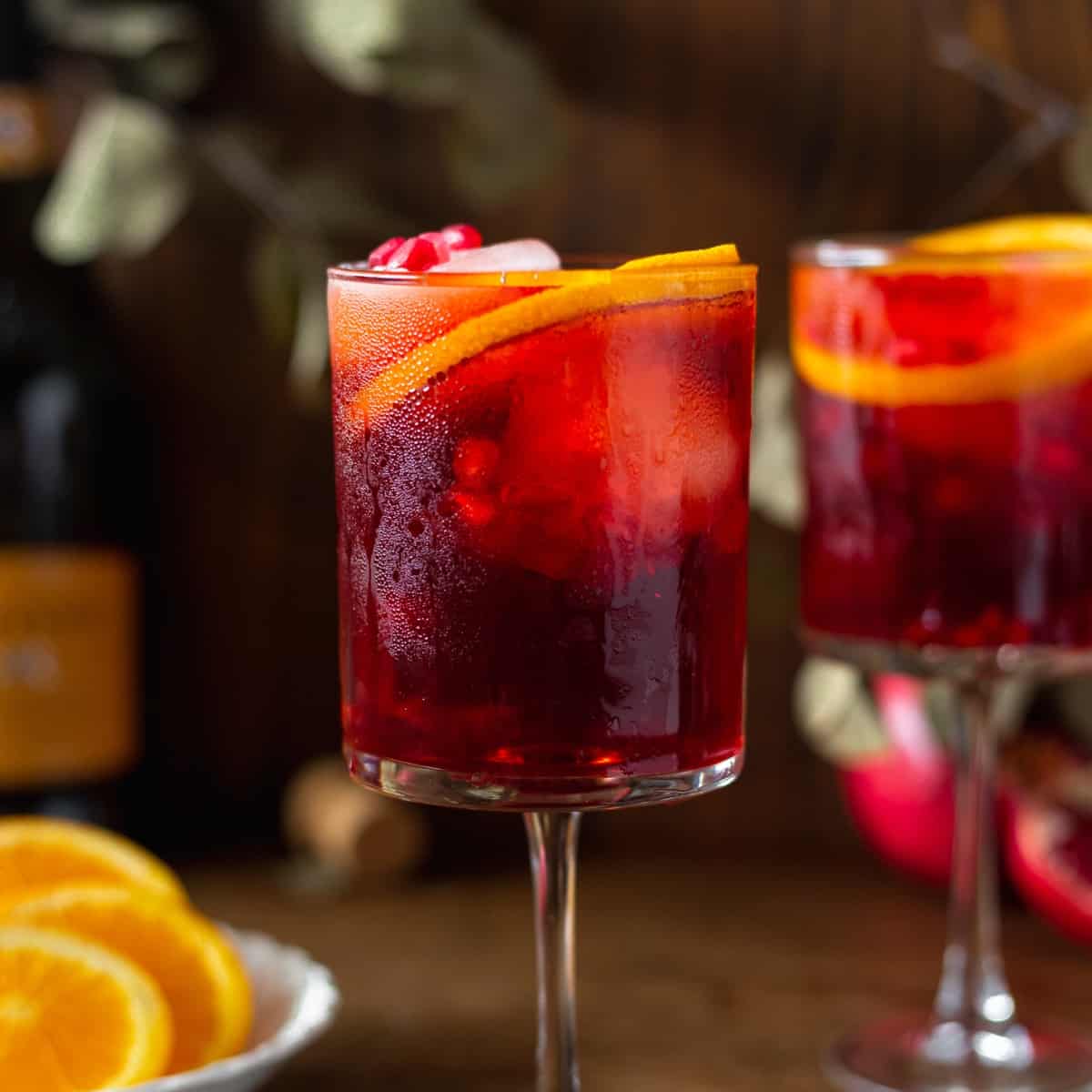 A square martini glass with a aperol spritz in it and pomegranate seeds