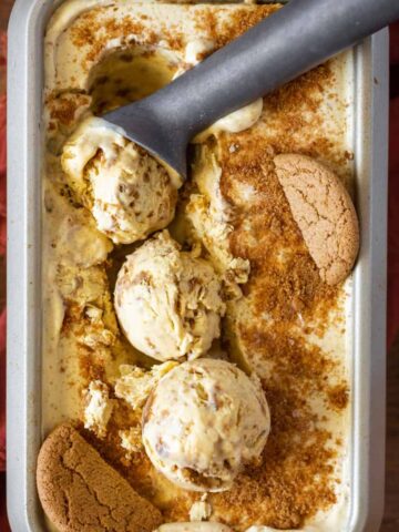 Container of pumpkin cheesecake ice cream with scoops of ice cream on top and gingersnap cookies
