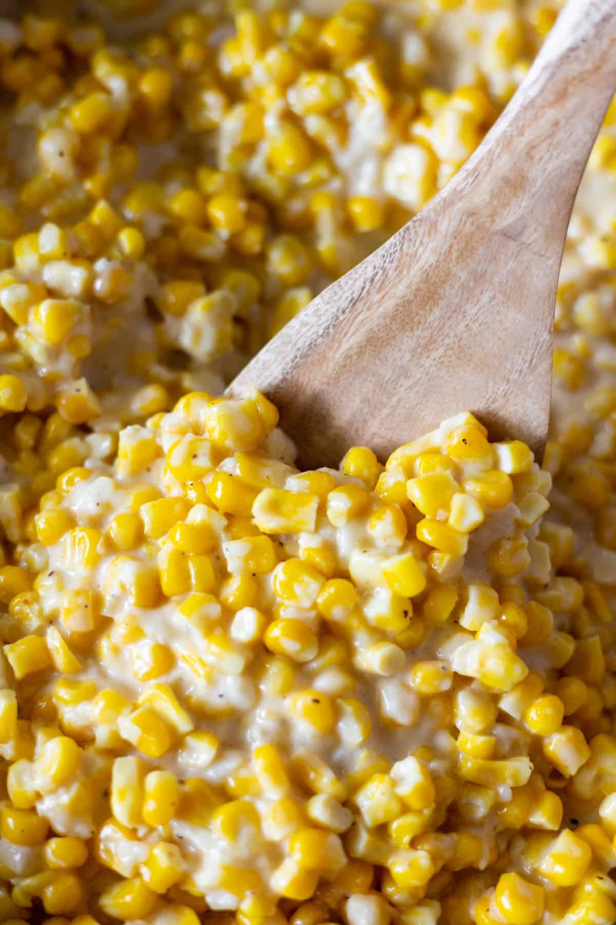 A close up shot of creamed corn with a wooden spoon in the center