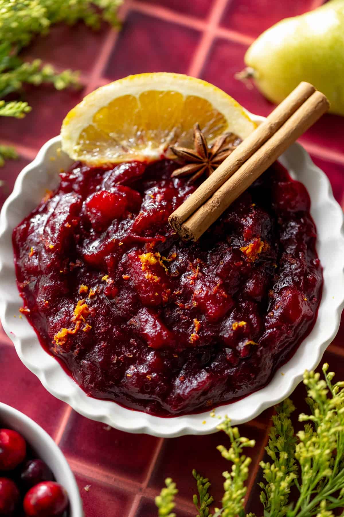 a white ruffled bowl with cranberry sauce and a cinnamon stick