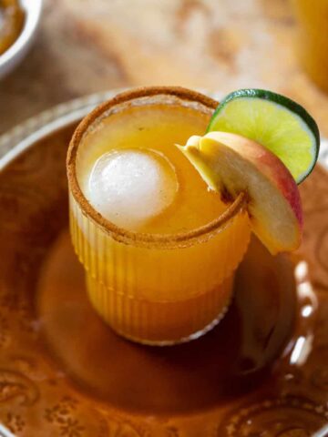Margarita in a cocktail glass with a lime and peach wedge.