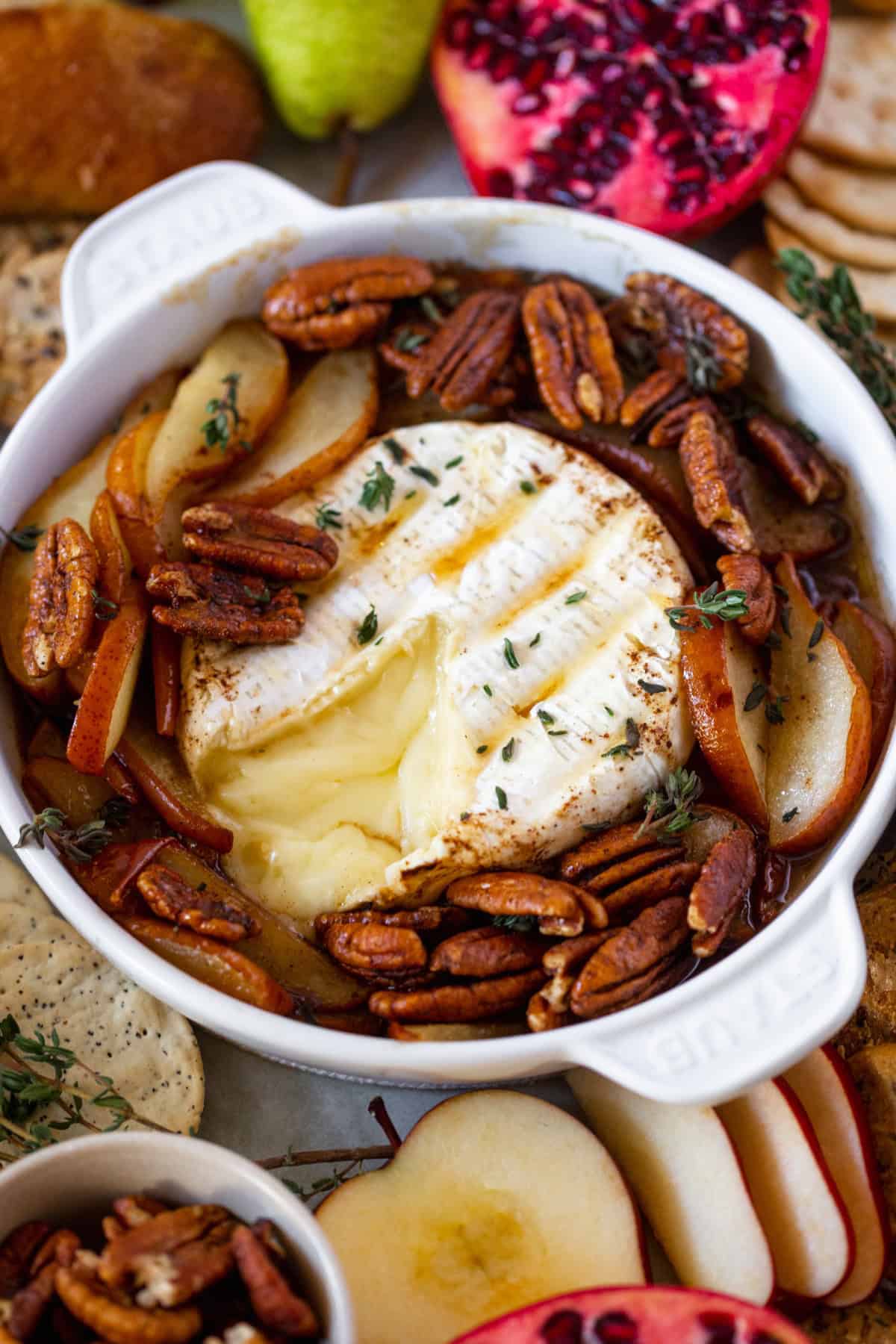 A slice of brie taken out of hot melted brie with pomegranates and grapes on the side